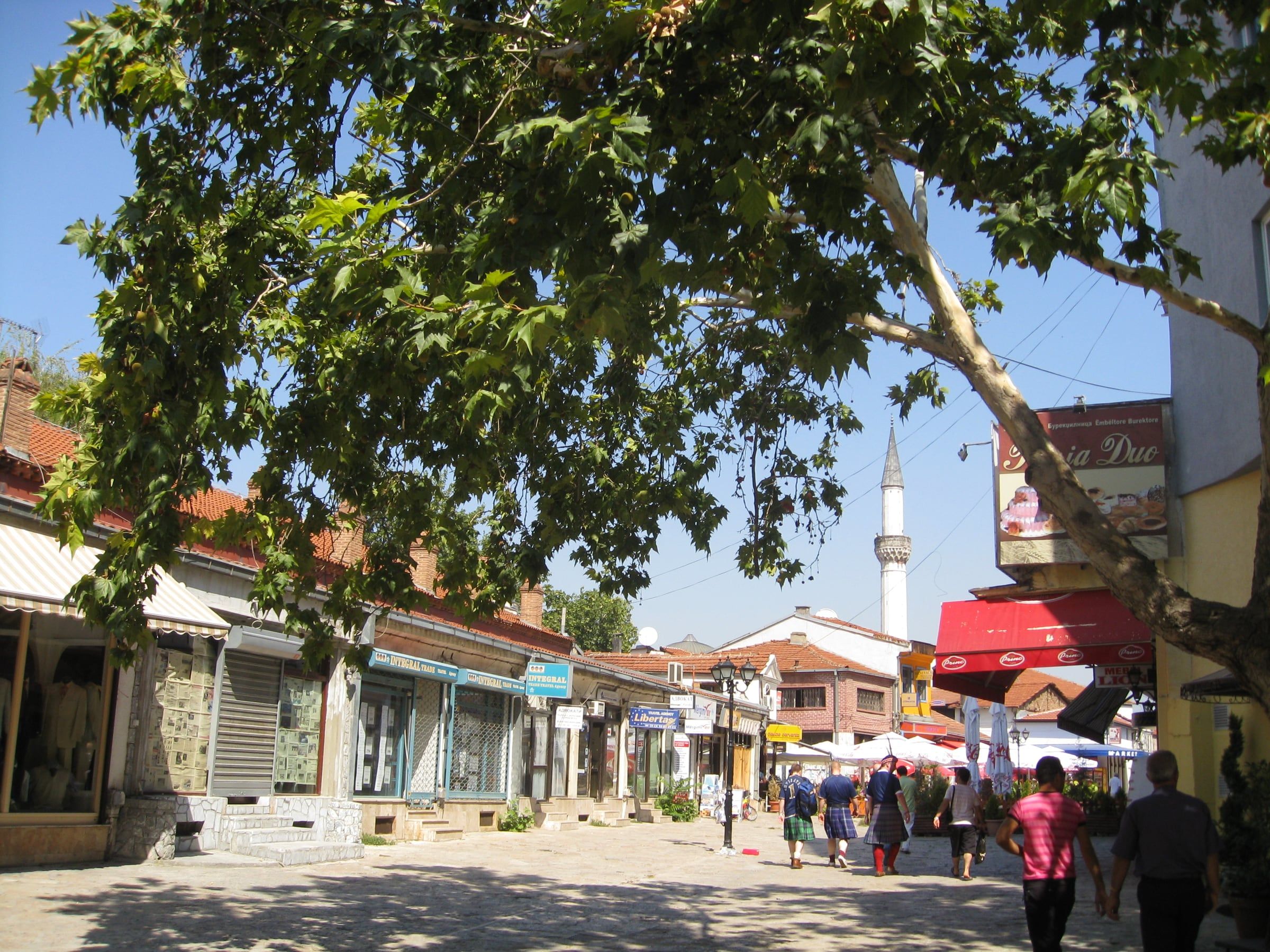 Cobbled old bazaar street lined with shops and a plane tree, with a minaret rising above the rooftops.